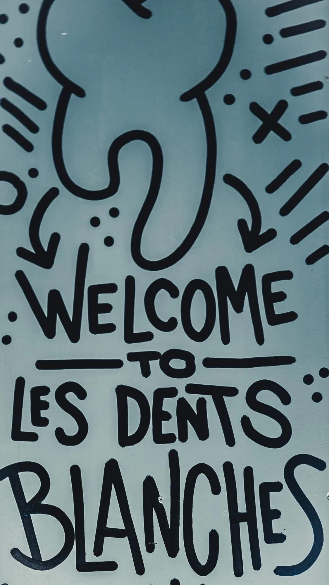 Hand-painted sign reading “Welcome to Les Dents Blanches” with doodled arrows