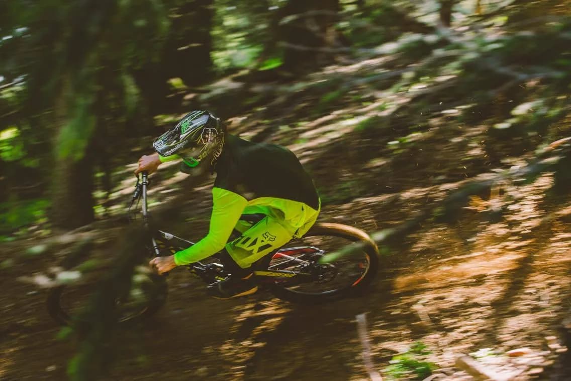 A mountain biker in a fluorescent green jersey riding through woodland.