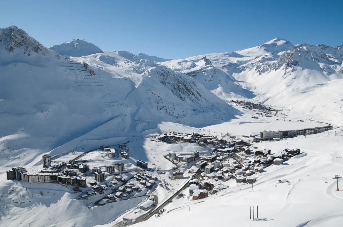 Luftaufnahme der Gebäude des Skiorts Tignes in einem verschneiten Bergtal unter blauem Himmel