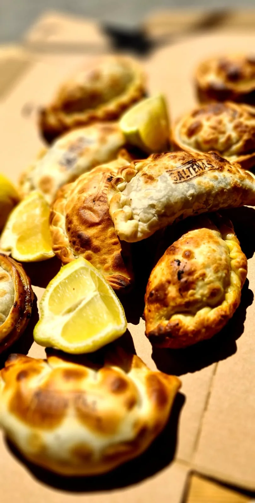 Goldbraun gebackene Empanadas mit Zitronenspalten auf einem Karton