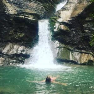 Swimmer floating on their back in a green pool beneath a waterfall