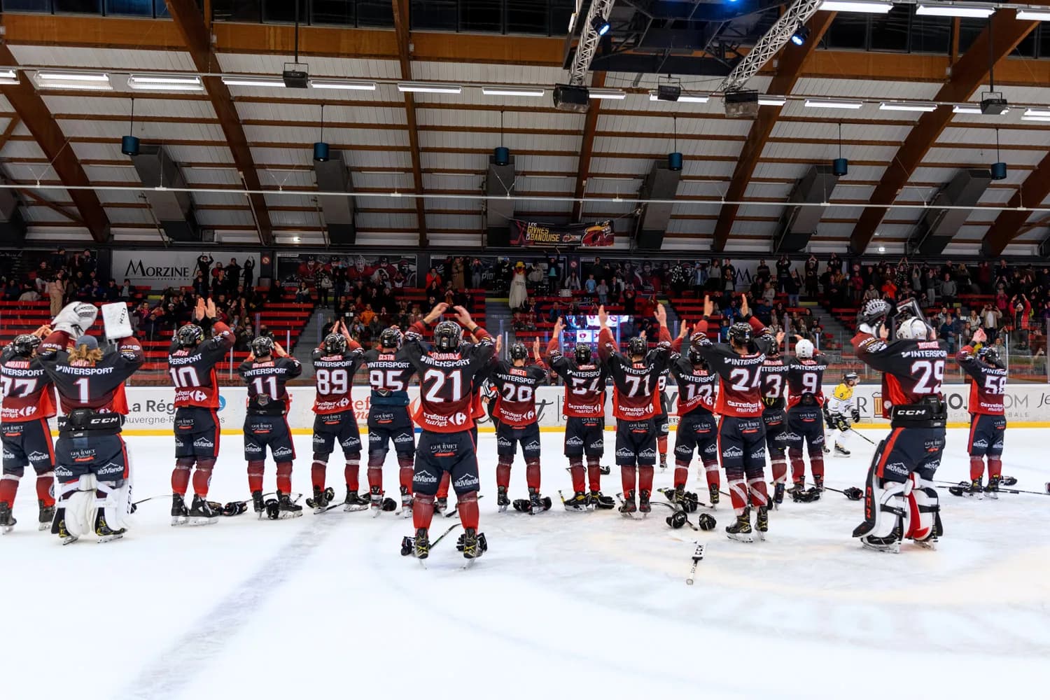 Das Eishockeyteam The Penguins in roten Trikots hebt auf dem Eis die Arme zum Publikum