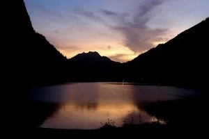 Silhouetted mountains around a lake at dusk under an orange and purple sky