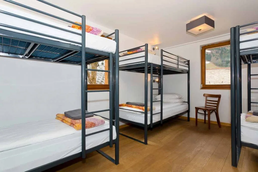 Hideout-Schlafsaal mit Metall-Etagenbetten, weißer Bettwäsche, Holzboden und Fenster