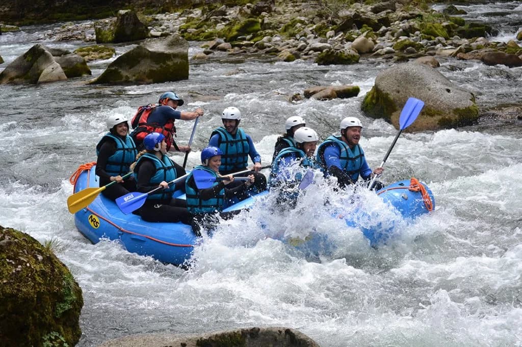 Gruppe mit Helmen und Schwimmwesten paddelt in einem blauen Schlauchboot durch Wildwasser