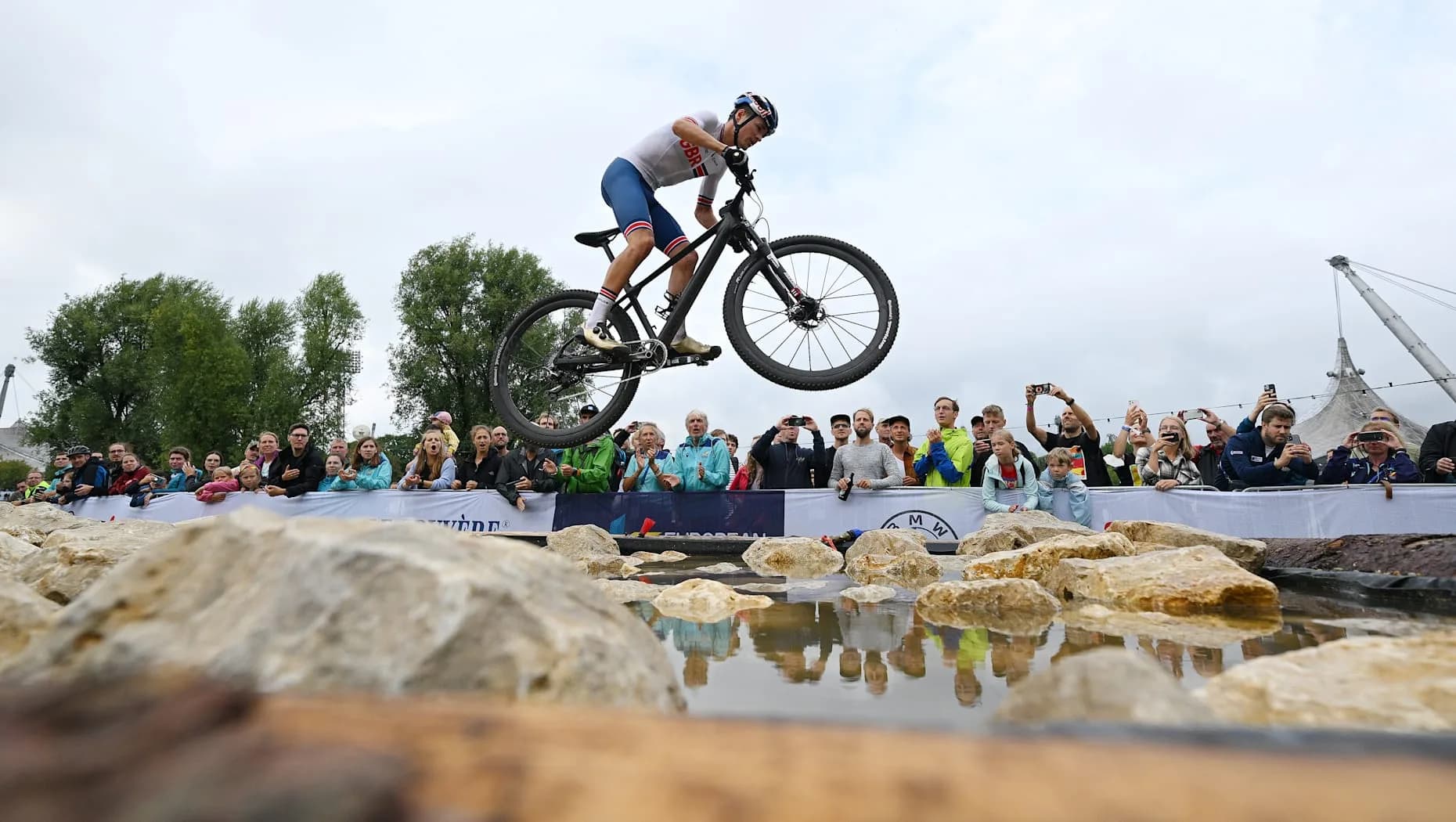 Mountain biker jumping over a rocky obstacle while spectators watch from behind barriers