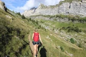 Hiker with a red backpack walking along a mountain path towards rocky cliffs