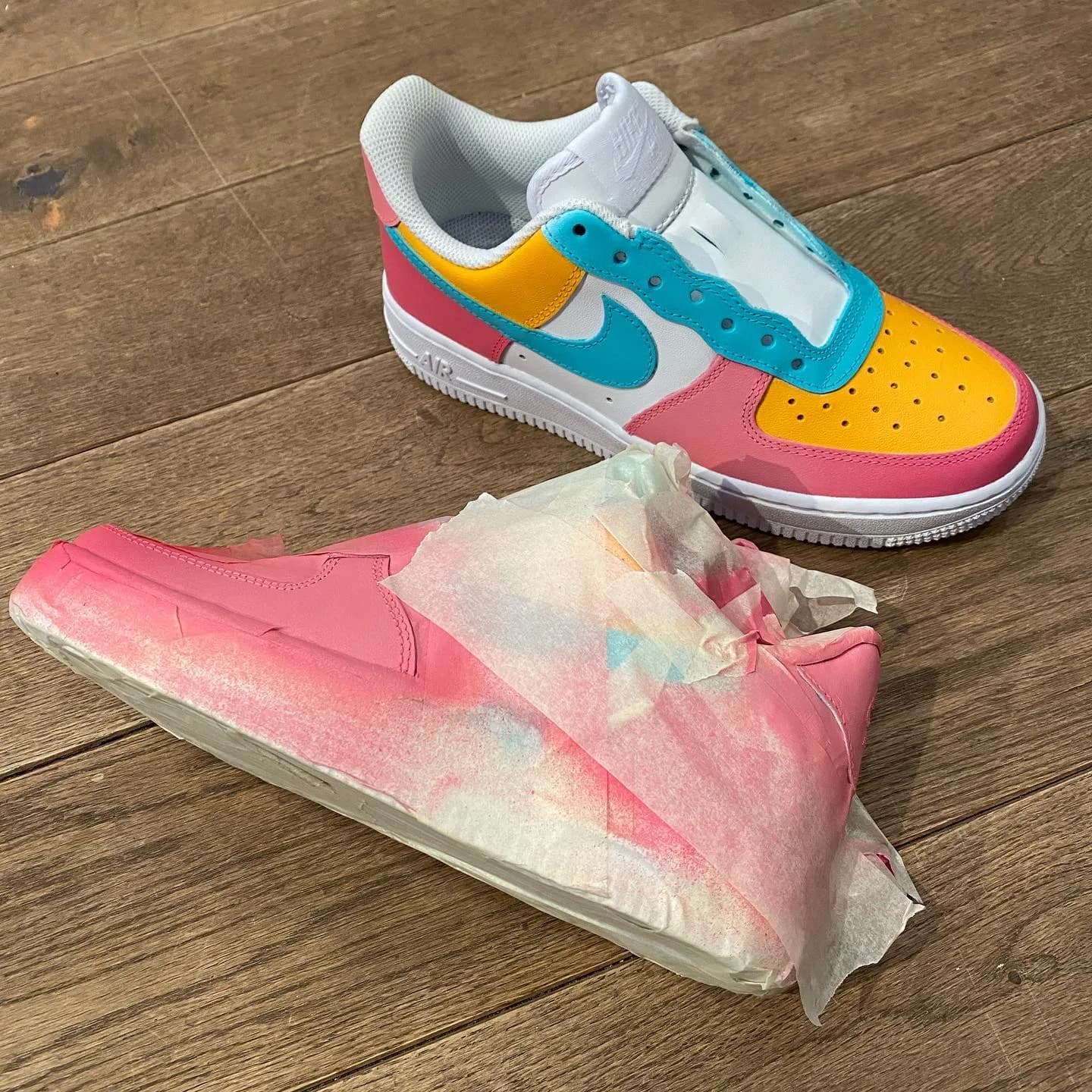 Custom-painted sneakers, one finished in pink, yellow and teal, the other masked with tape and paint