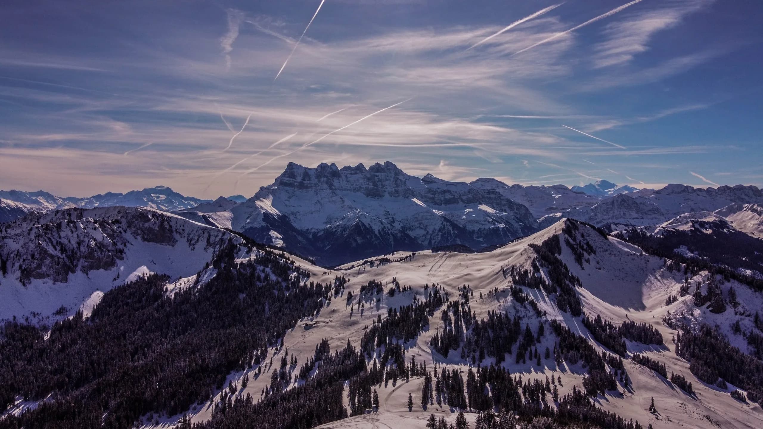 Verschneite Bergkämme und eine schroffe Gipfelkette unter blauem Himmel mit Kondensstreifen