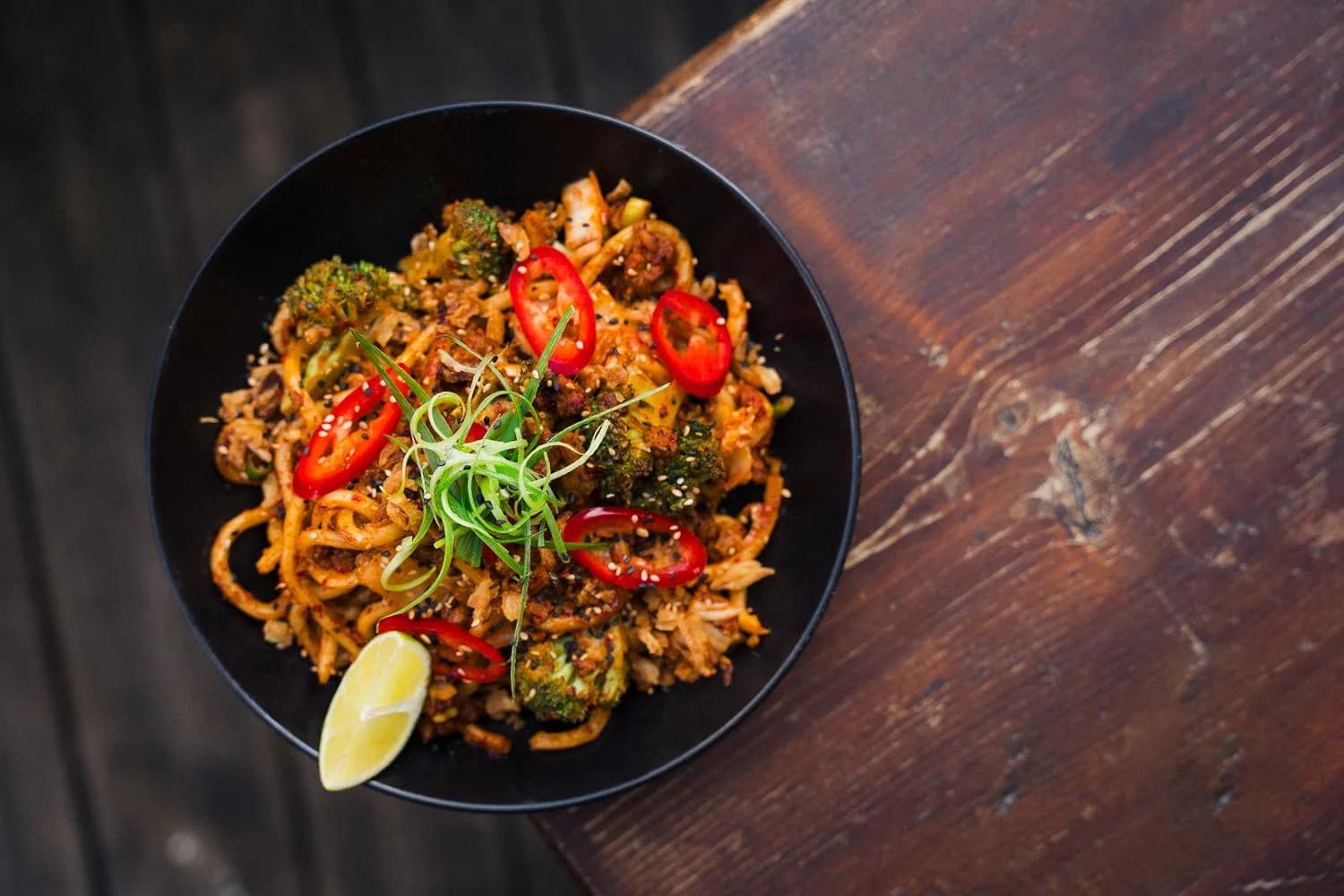 Eine Schüssel Nudeln mit roten Chilis, Grünzeug und Limette