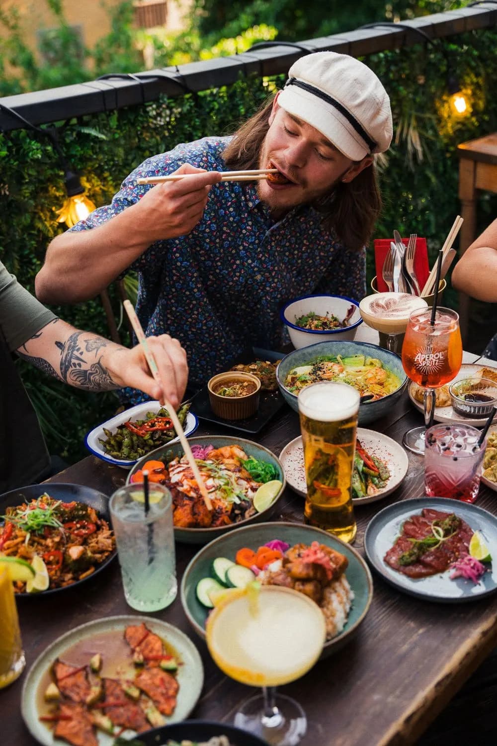 Ein Gast isst mit Stäbchen an einem Tisch voller Essen und Drinks