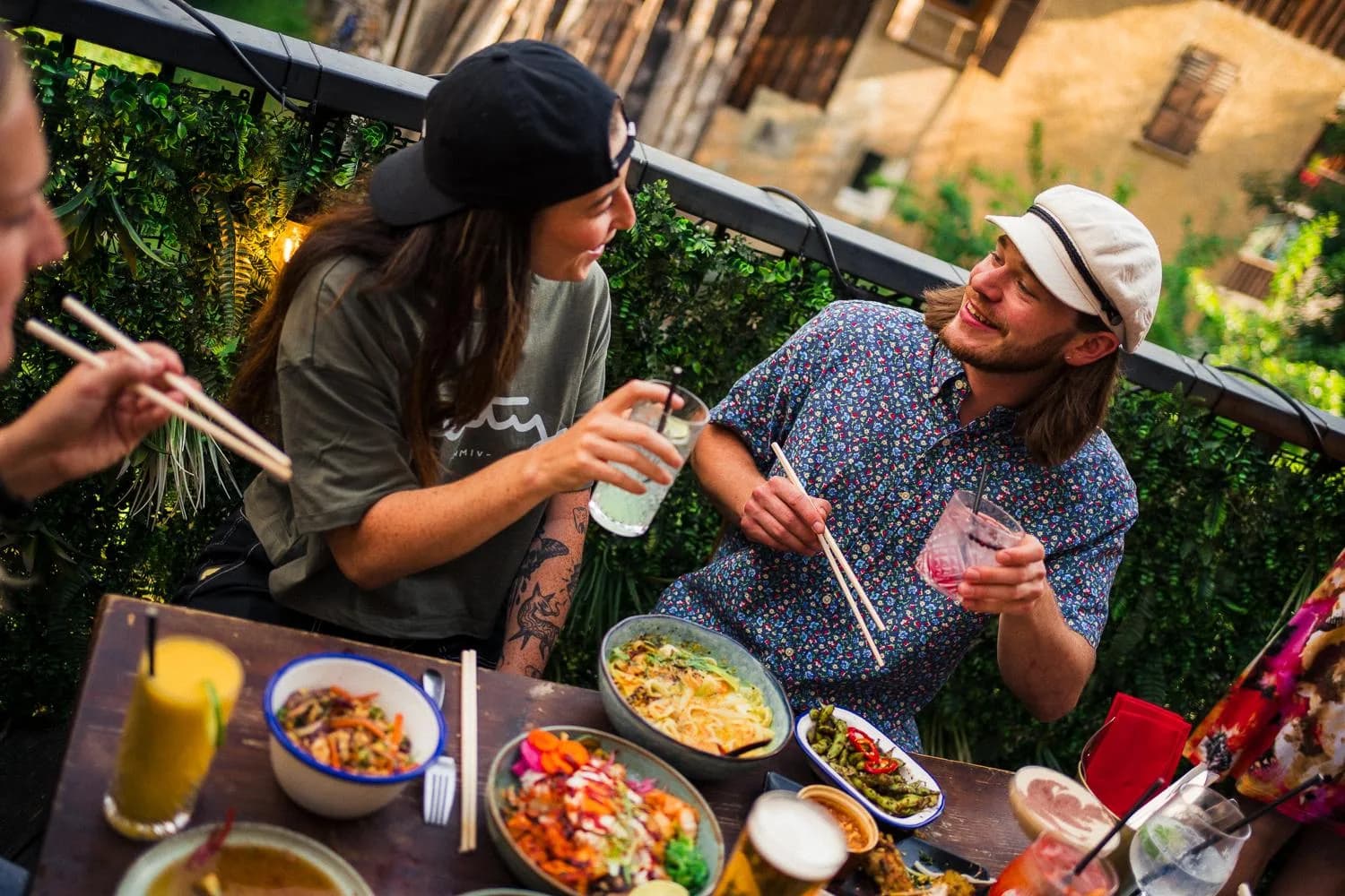 Freunde lachen zusammen beim Teilen von Gerichten auf der Hideout-Terrasse