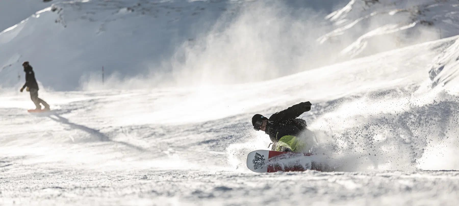 Ein Snowboarder carvt durch frischen Pulverschnee hoch über Morzine