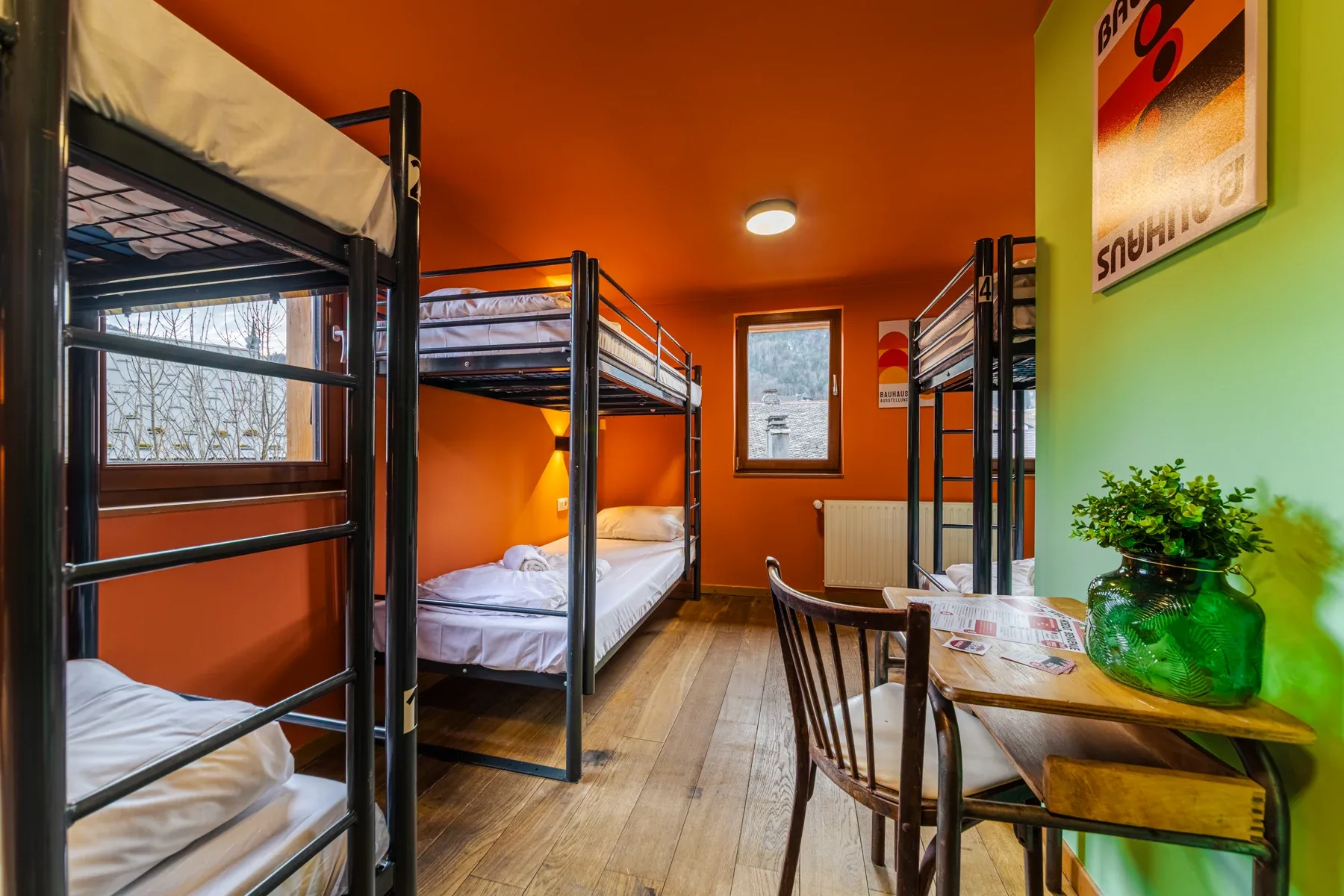Sechsbett-Schlafsaal mit Metall-Etagenbetten, orangefarbener Decke und grüner Wand